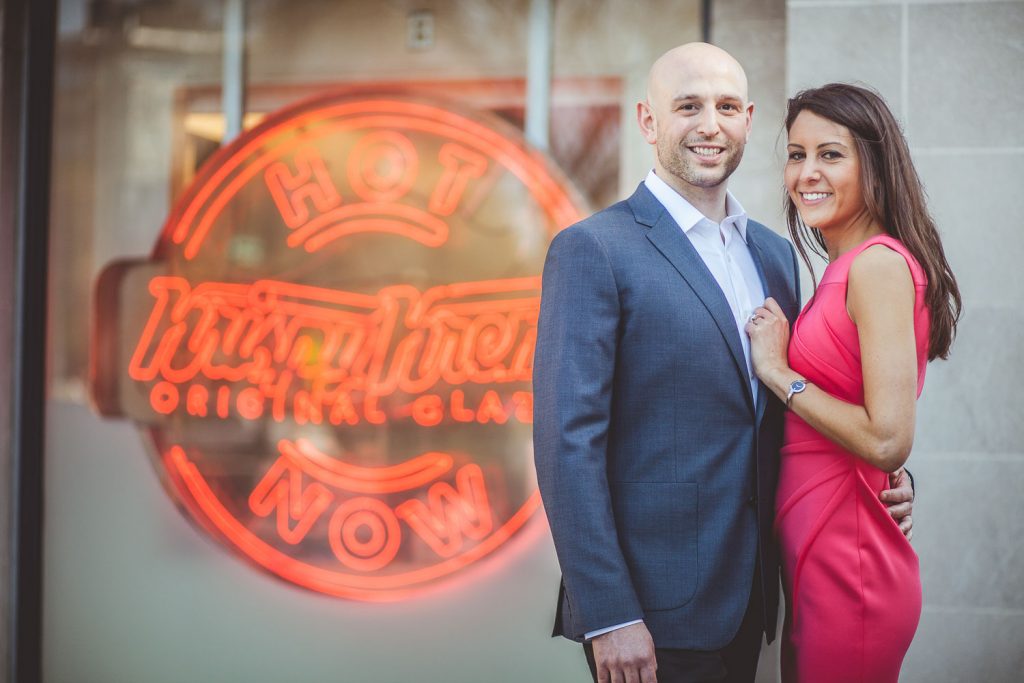 Engaged couple in front of Krispy Kreme sign at Dupont Circle in DC.