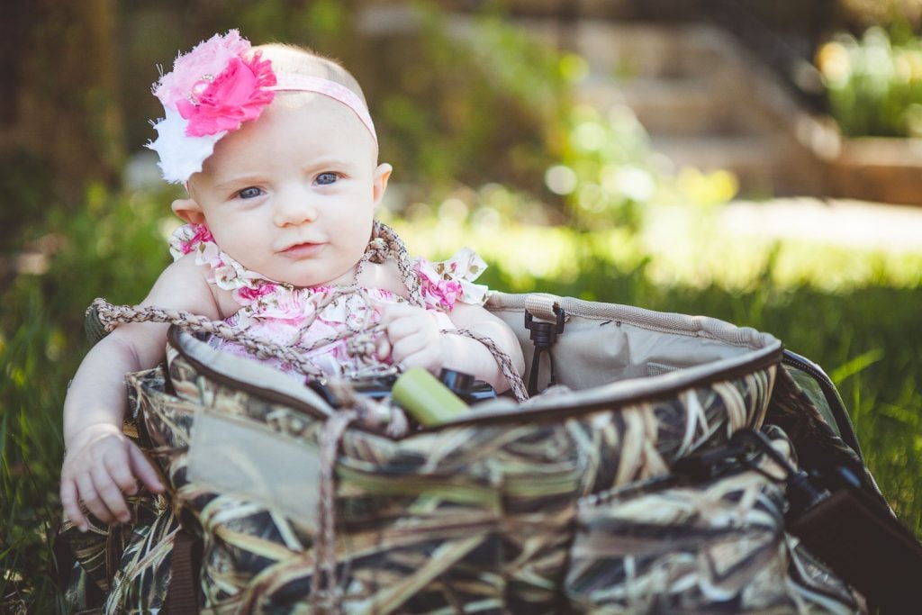 A scene featuring a camouflaged hunting bag, could be seen as contrasting the flowery baby dress, or when considering the baby is in the bag, it could be seen as complementing.