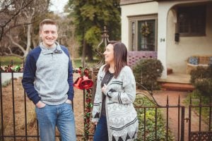 A couple standing in front of a fence adorned with Christmas decorations, capturing a wholesome portrait in Downtown Annapolis.