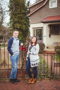 A couple standing in front of a house adorned with twinkling Christmas lights.