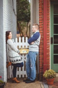 A engaged couple posing for a portrait against a white picket fence in Downtown Annapolis.