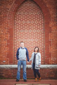 An engaged couple stands together in front of a brick wall in downtown Annapolis.