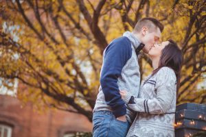 A portrait of an engaged couple kissing in front of a brick wall in Downtown Annapolis.