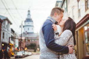 A couple kisses in front of a clock tower during their engagement session in Downtown Annapolis.