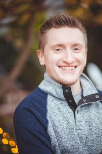 A young man smiling in front of a tree in Downtown Annapolis.