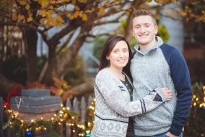 A couple posing in front of a fence adorned with Christmas lights, capturing their portrait in the enchanting ambiance of Downtown Annapolis.