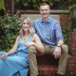 An engaged couple sitting on bricks in Downtown Annapolis, capturing a beautiful engagement photo in a garden.