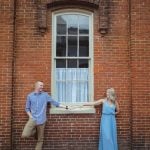 An engagement photo of a couple holding hands in front of a brick building in downtown Annapolis.