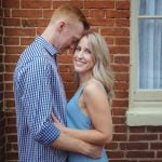 An engaged couple embracing in front of a brick wall in downtown Annapolis, capturing a beautiful engagement photo portrait.