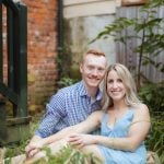 An engaged couple having a portrait taken in Downtown Annapolis, sitting in the grass in front of a brick building.