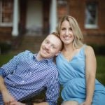 An engaged couple posing in front of a brick house for their engagement photo.