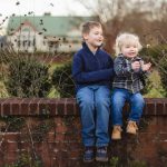 Two boys sitting on a brick wall in front of a brick wall during an engagement session at Quiet Waters Park.