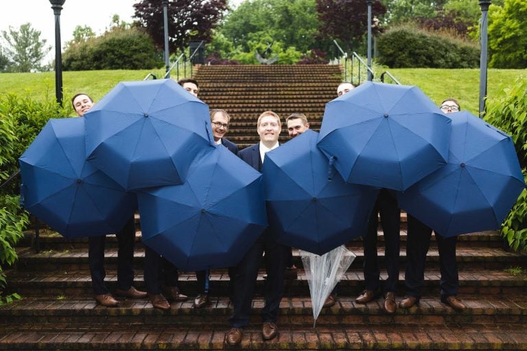 A group of groomsmen holding umbrellas on steps at Quiet Waters Park in Annapolis, Maryland.