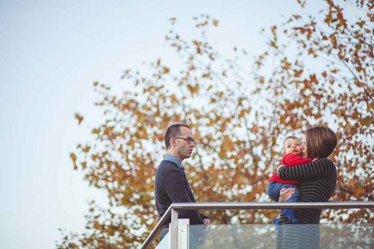 A family is standing on a railing at Yards Park with a baby in their arms.