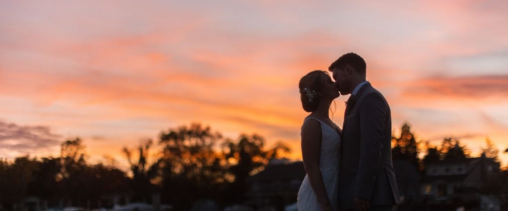 A bride and groom kiss in front of a sunset at Anchor Inn, Maryland.