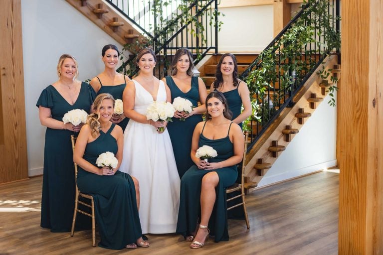 A bride and her bridesmaids posing in front of a staircase at Atreeum at Soaring Timbers in Maryland.