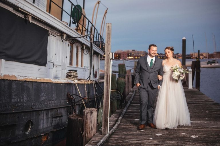 A bride and groom at Baltimore Museum of Industry standing on a dock next to a boat.