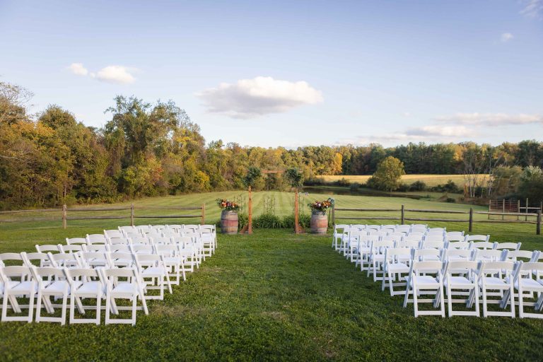 A wedding ceremony set up in a field at the Barns at Hamilton Station Vineyards with white chairs.