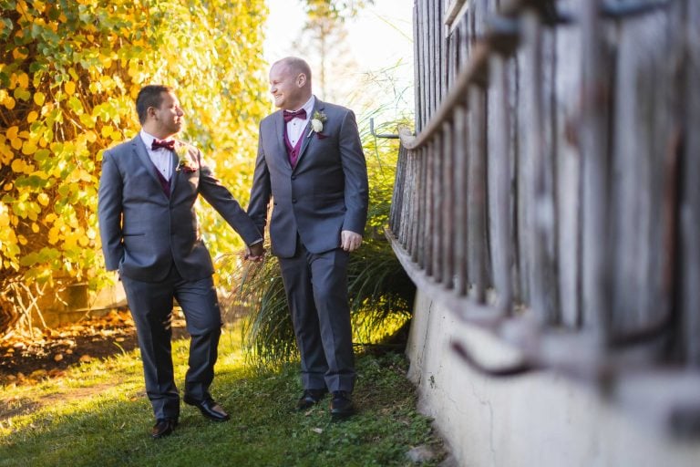 Two grooms holding hands in front of the Barns at Hamilton Station Vineyards in Virginia.