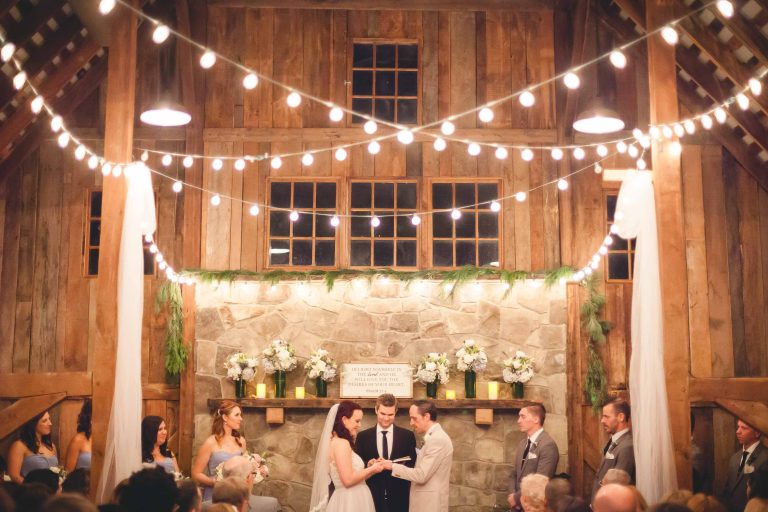 A wedding ceremony in a rustic barn adorned with string lights at Barns at Hamilton Station Vineyards in Hamilton, Virginia.