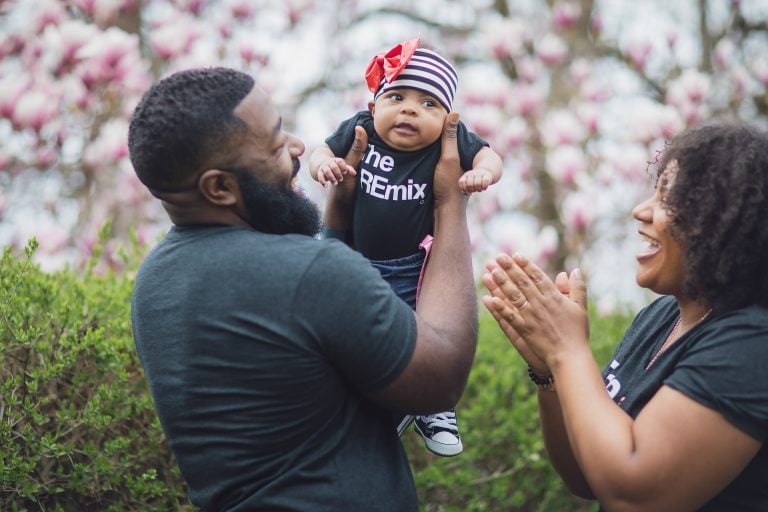 A family holding a baby in front of pink flowers at Belair Mansion in Maryland.