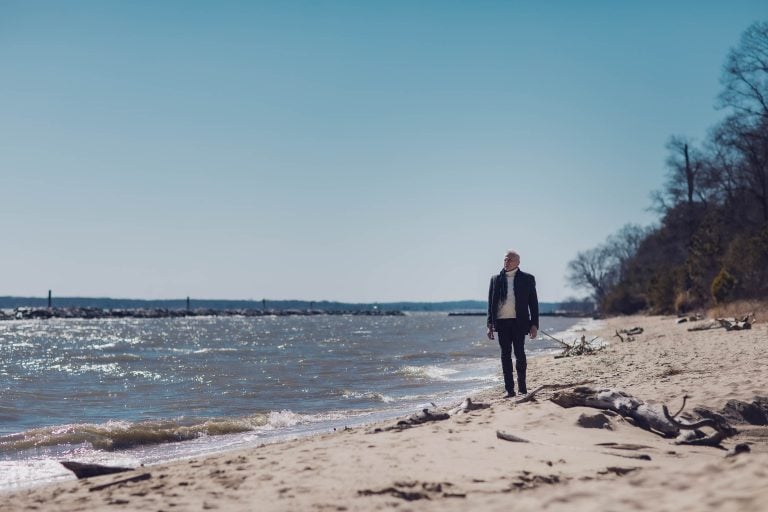 A man walking on a beach near the water at Beverly Triton Nature Park in Maryland.