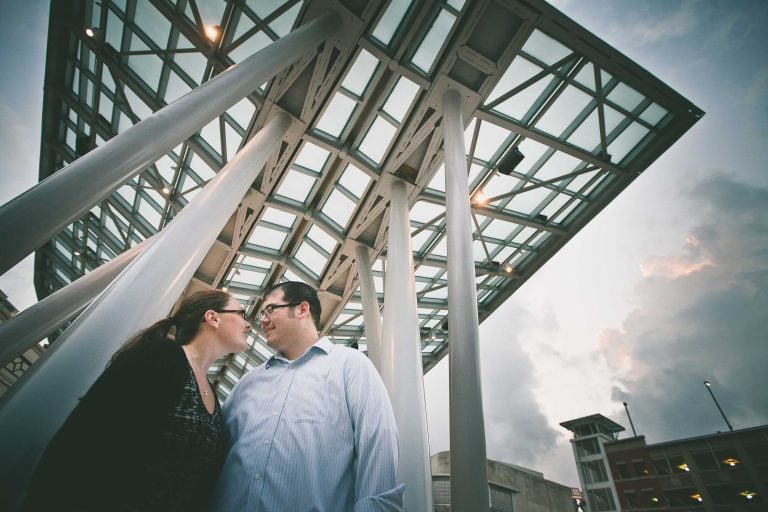 An engaged couple standing in front of a glass structure in Downtown Silver Spring.