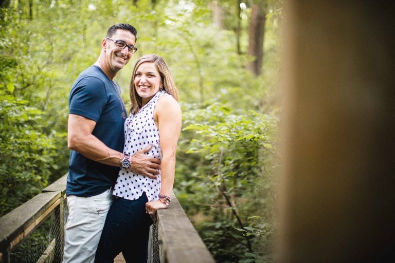 An engaged couple standing on a wooden bridge at Irvine Nature Center in Owings Mills, Maryland.