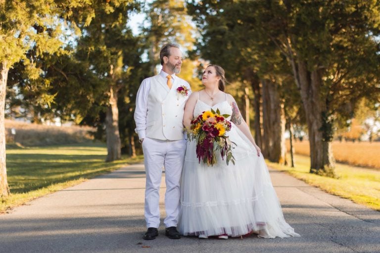 A bride and groom standing on a road at Jefferson-Patterson Park in Maryland, with trees in the background.