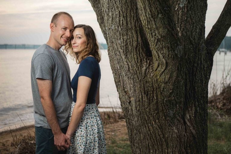 A couple is posing in front of a tree near the water at Jonas and Anne Catharine Green Park in Annapolis, Maryland.