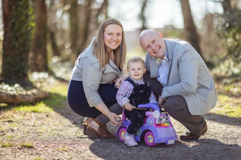 A man and woman pose with a little girl in a purple toy car at Jones Point Park in Alexandria, Virginia.