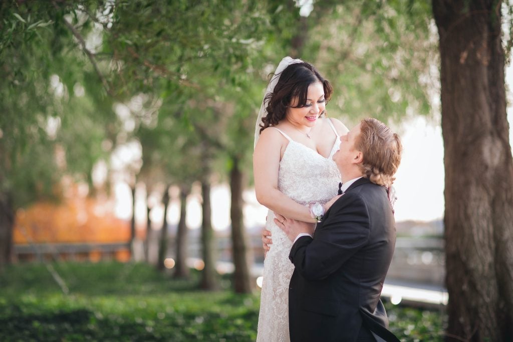 A bride and groom hugging in front of a tree at the Kennedy Center Grounds.