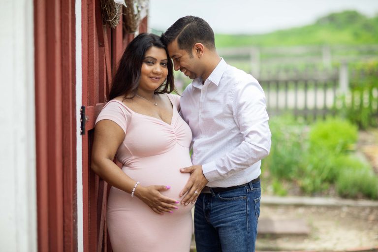 A pregnant couple posing in front of a barn at Kinder Farm Park in Millersville, Maryland.