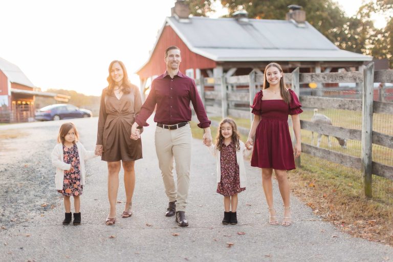 A family walks down a country road holding hands in front of Kinder Farm Park barn.