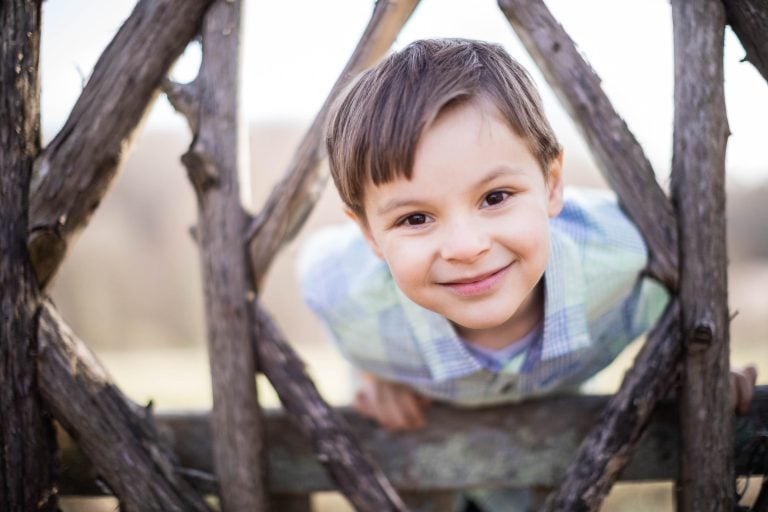 A young boy is leaning over a wooden fence at Meadowlark Botanical Gardens in Vienna, Virginia.