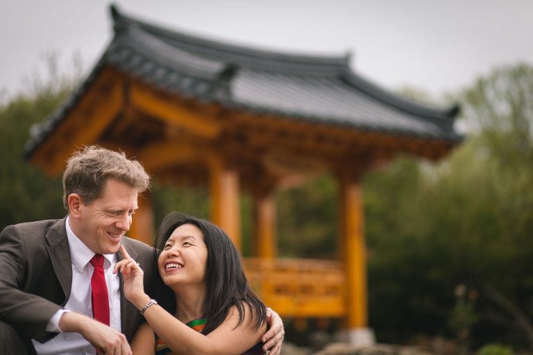 A man and woman are posing in front of a Japanese pagoda at Meadowlark Botanical Gardens in Vienna, Virginia.