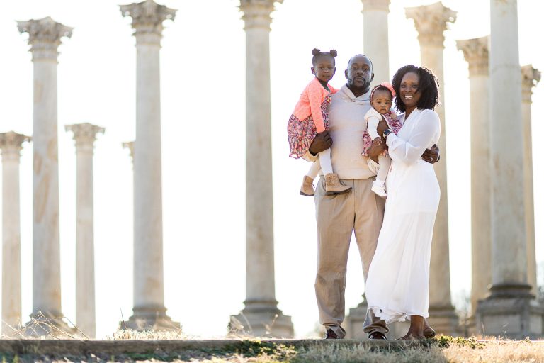 A family is posing in front of a group of pillars at the National Arboretum.