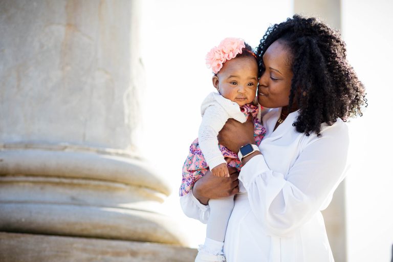 A woman holding a baby in front of columns at the National Arboretum.