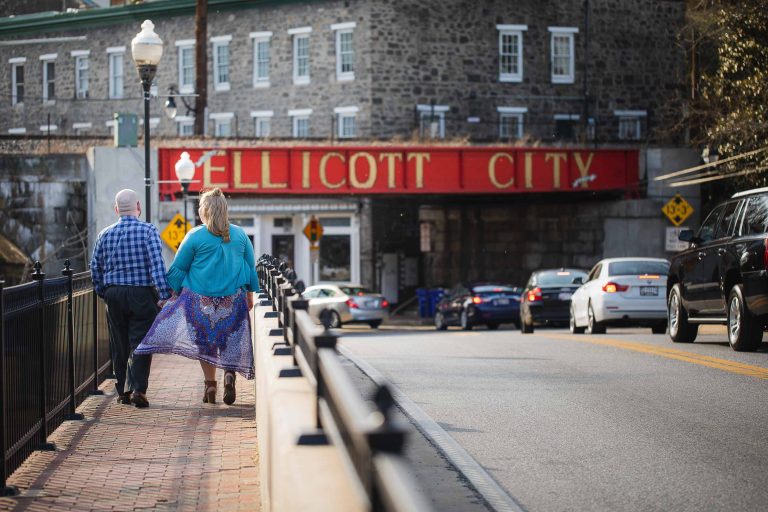 A couple walking down a street in Old Ellicott City with a sign that says Ellicott City, Maryland.