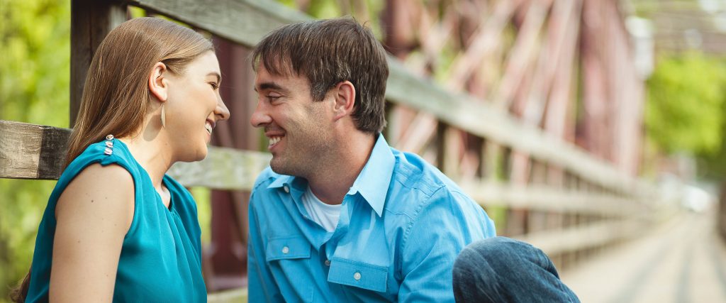 A man and woman are sitting on a wooden bridge at Historic Savage Mill in Maryland.