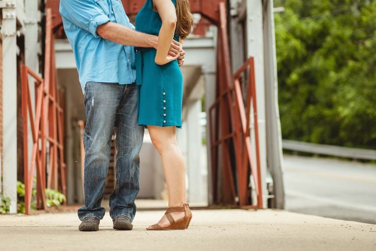 A man and woman hugging in front of a historic bridge.