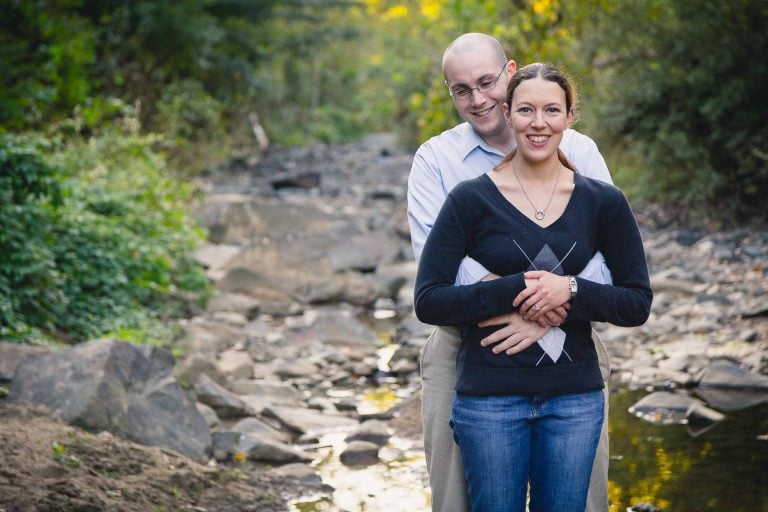 A man and woman are posing in front of a stream at Historic Savage Mill in Maryland.