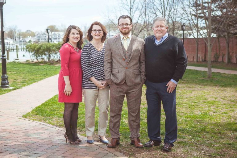 Four people posing for a picture in front of a brick walkway at Acton's Cove Waterfront Park in Annapolis, Maryland.