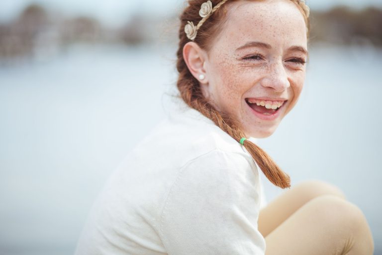 A young girl is smiling while sitting on a dock at Acton's Cove Waterfront Park in Annapolis, Maryland.