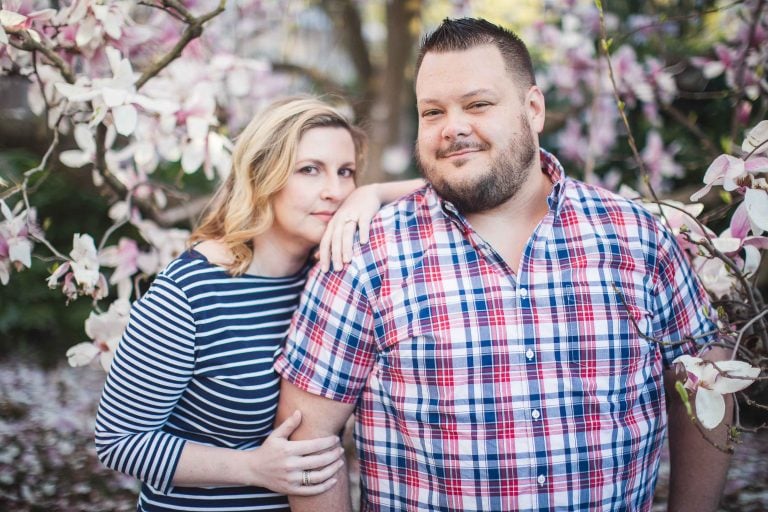 An engaged couple posing in front of magnolia blossoms at Enid Haupt Garden in Washington DC.