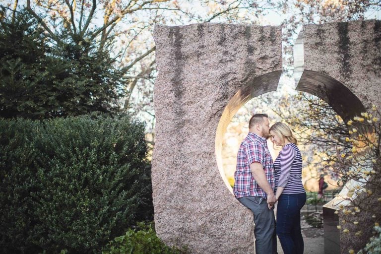 An engaged couple standing in front of a stone sculpture in Washington DC.