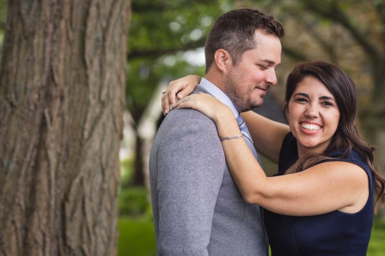 An engaged couple hugging in front of a tree at Hayfields Country Club in Maryland.