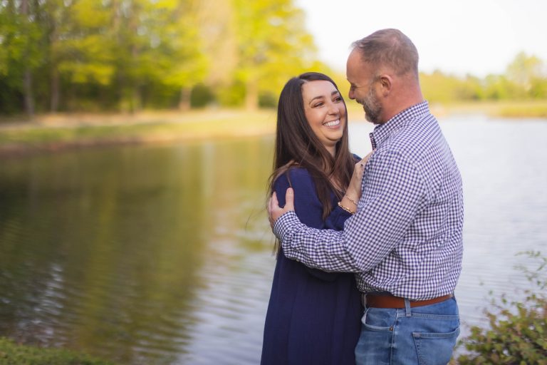 An engaged couple embracing in front of Mill Branch Pond in Maryland.