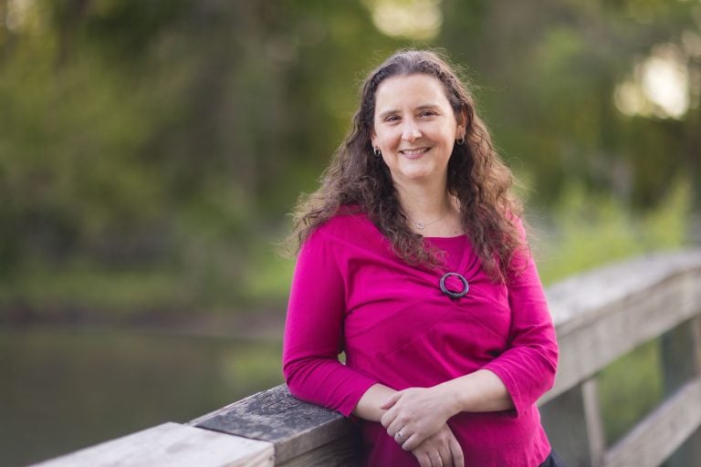 A woman in a pink shirt is leaning on a wooden bridge at Mill Branch Pond.