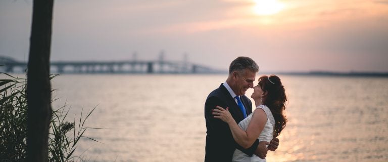 A couple embracing in front of the water at sunset at Terrapin Nature Park in Maryland.